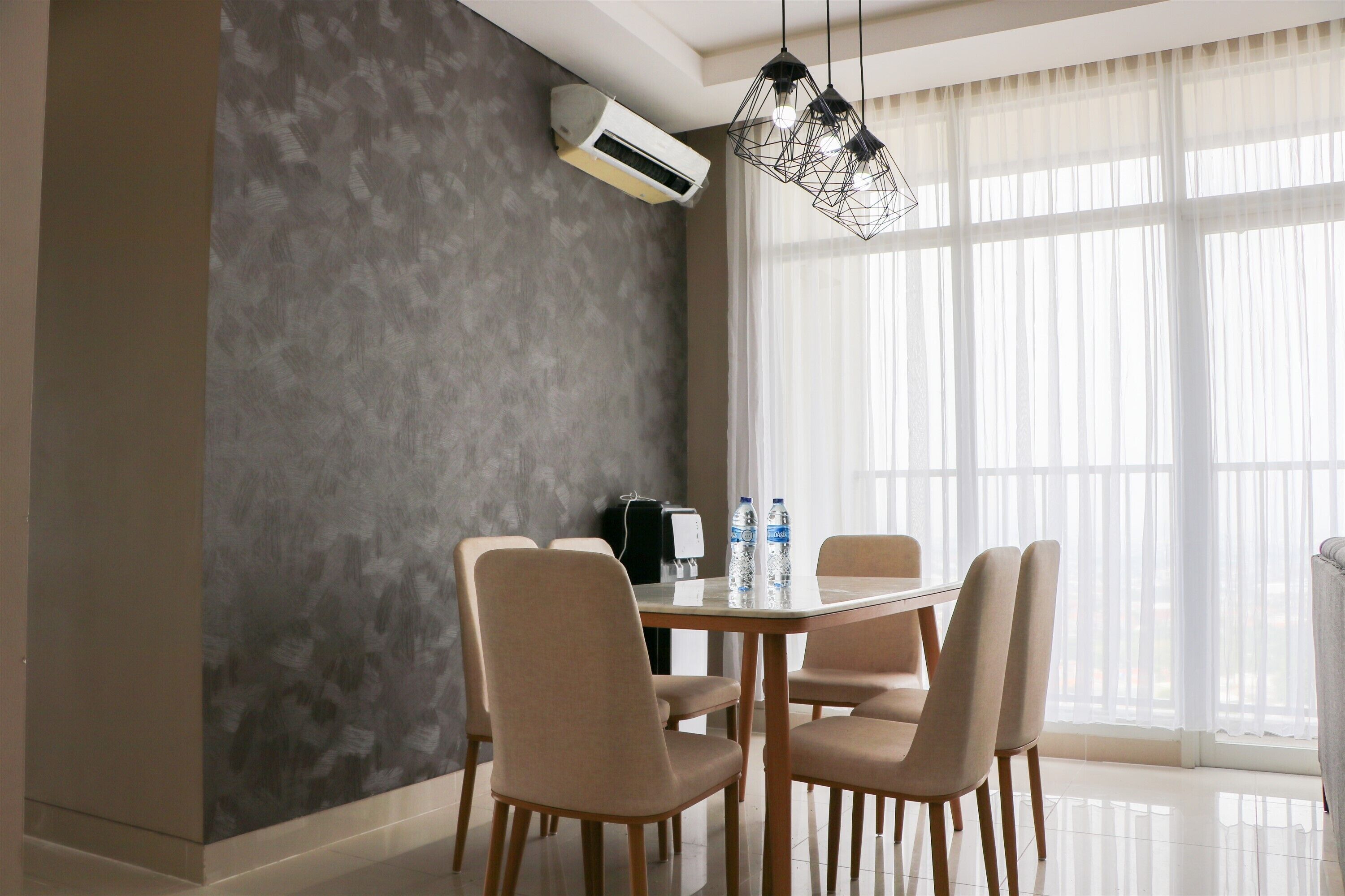 Un comedor moderno con una mesa, sillas, un equipo de aire acondicionado y un ventanal con cortinas translúcidas.