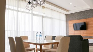A modern hotel room with a dining area, a sofa, and a flat-screen TV mounted on the wall. - Spacious And Comfy 3Br Ciputra International Apartment (Jakarta)