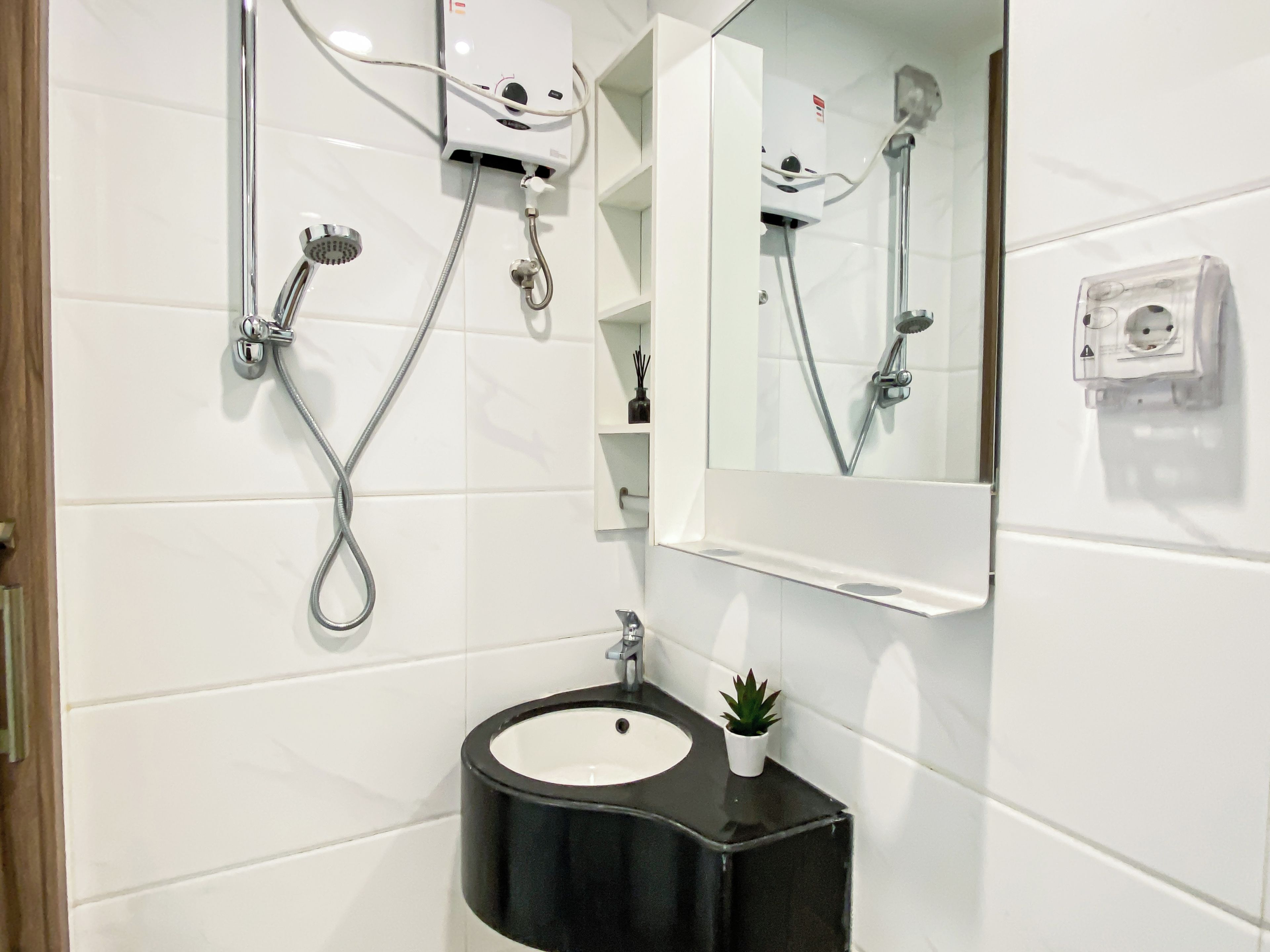 A bathroom with a black sink, a mirror, a handheld showerhead, and a wall-mounted heater.