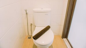 A white toilet with a shower attachment and a towel on the seat. - Warm And Simply Studio Room Sky House Alam Sutera Apartment (Tangerang)