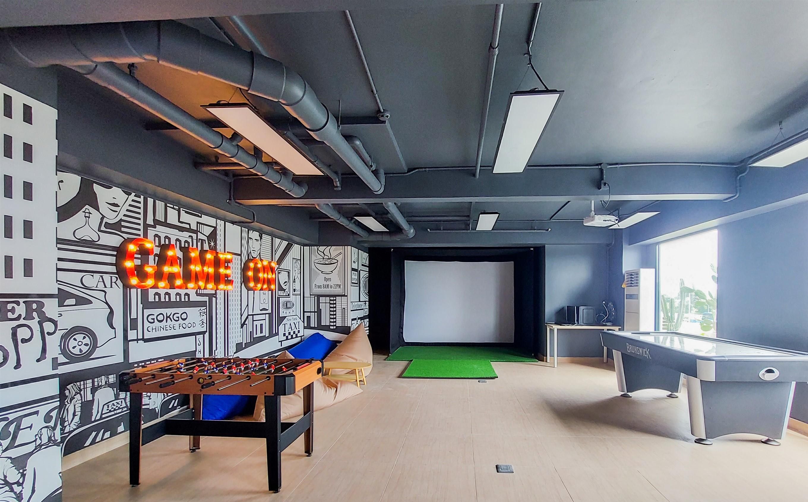 A room with a foosball table, a projector screen, and a foosball table with a green mat.