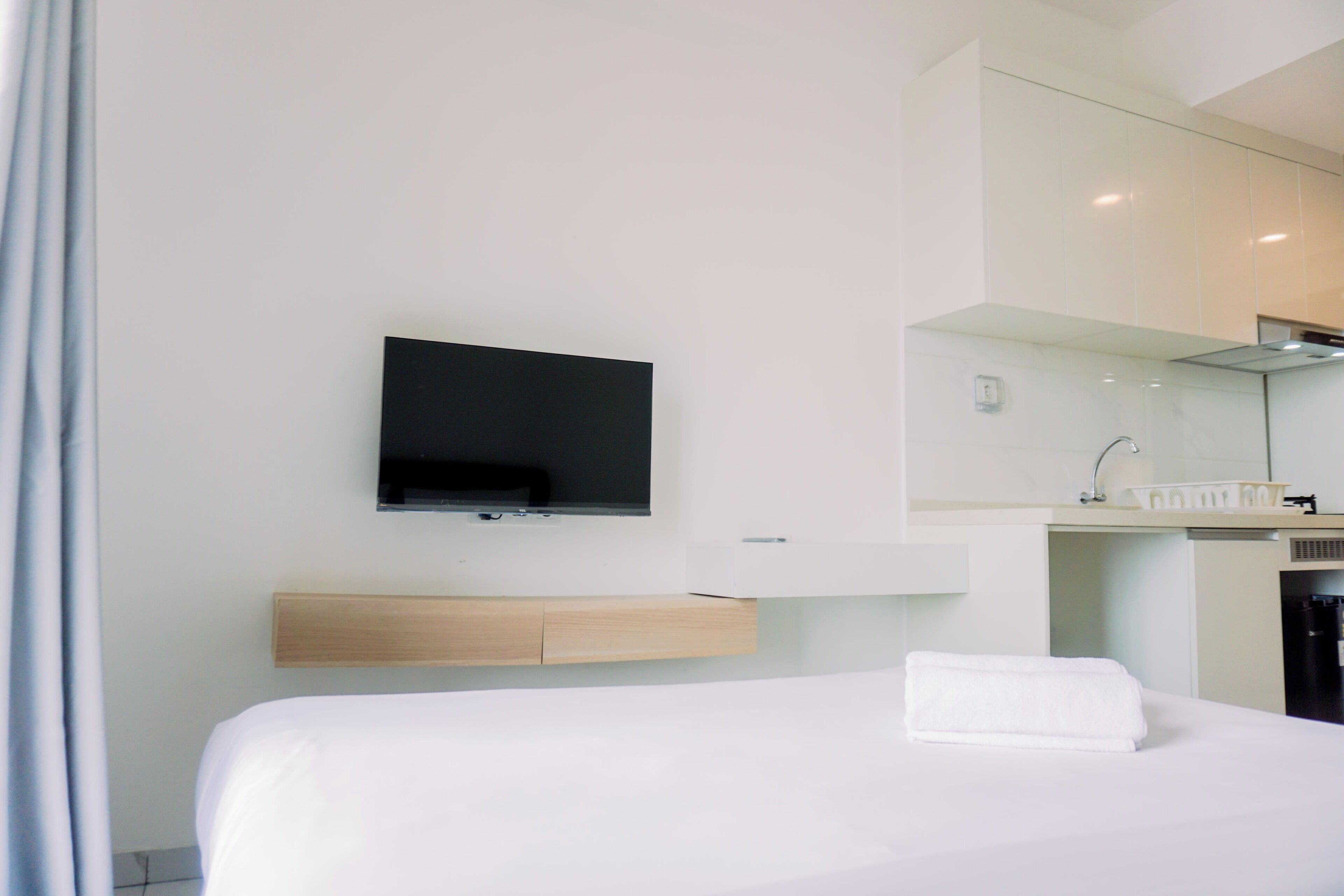 A modern hotel room with a bed, a mounted television, a wooden bedside table, and a bathroom with a mirror and sink.