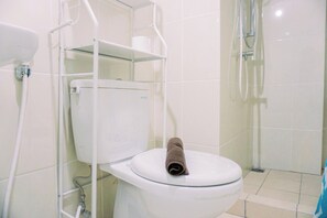 A bathroom with a white toilet, a glass shower enclosure, and a towel on the toilet seat. - Scenic And Homey 2Br Apartment M-Town Residence Near Mall (Gading Serpong)