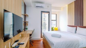 Una habitación de hotel moderna con una cama grande, un escritorio con televisor de pantalla plana, aire acondicionado integrado y ventana con vistas a la ciudad.