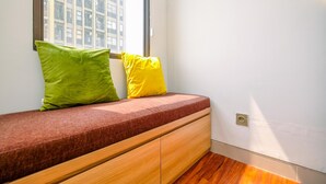 Una habitación de esquina con un banco empotrado en la pared, una ventana y suelo de madera.