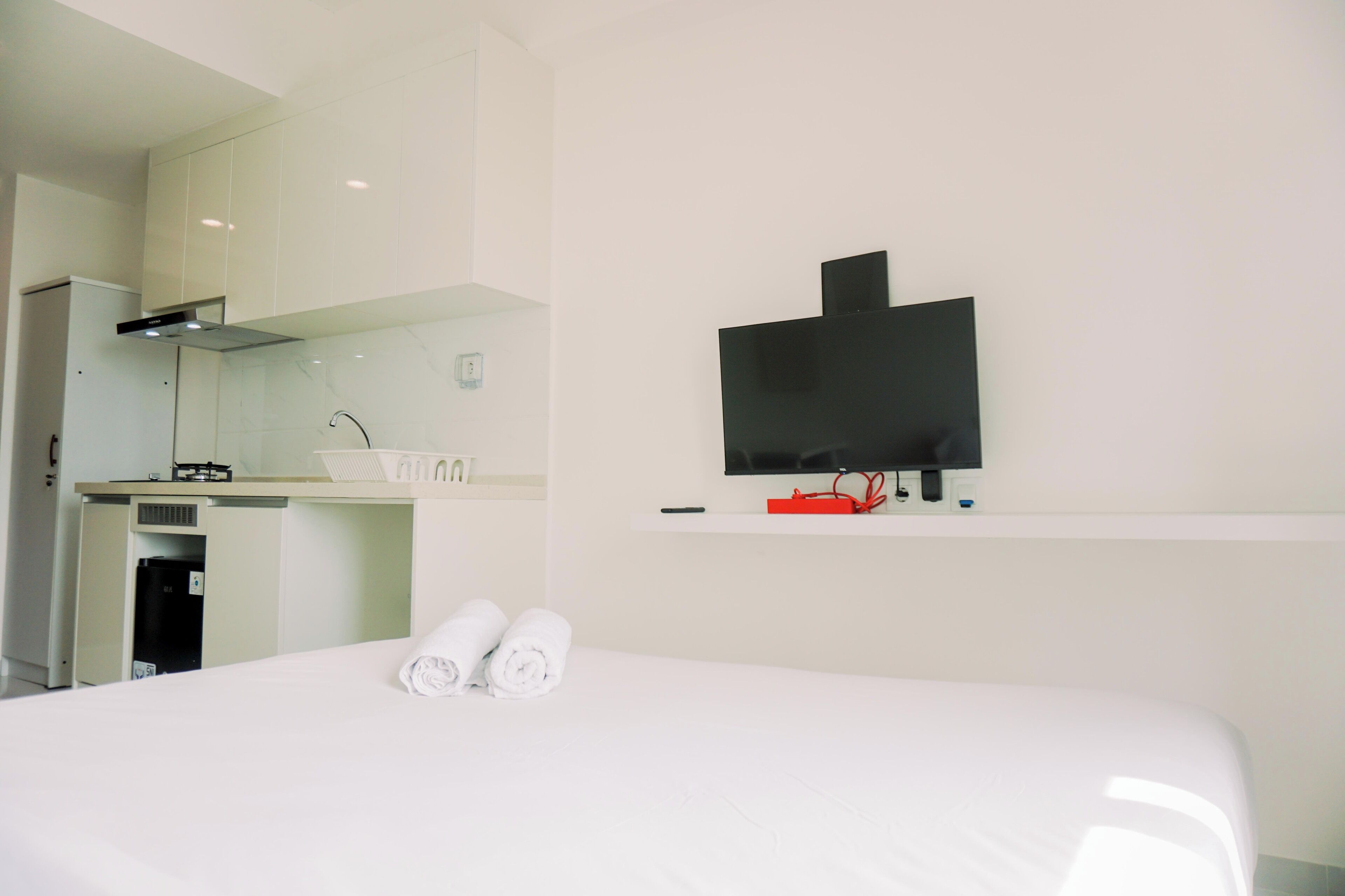 Ein Hotelzimmer mit einem Bett, einem an der Wand befestigten Fernseher, einer kleinen Küchenzeile und einem Spiegel.