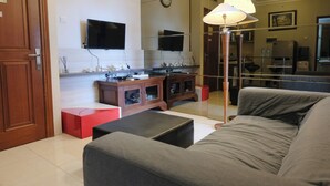 Una sala de estar con sofá, televisión, mueble y lámpara.