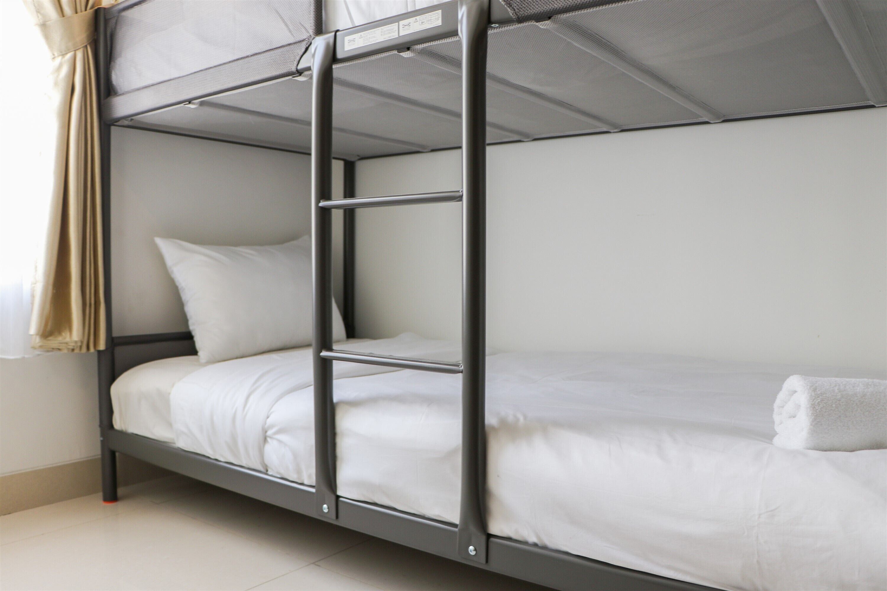 A bunk bed with a ladder, white bedding, and a rolled towel on the lower bunk.