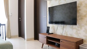 A modern room with a large flat-screen TV mounted on the wall, a wooden TV stand with a drawer, a door, and a curtain.