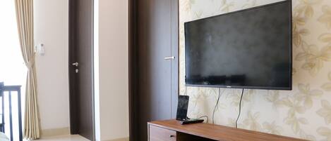 A modern room with a large flat-screen TV mounted on the wall, a wooden TV stand with a drawer, a door, and a curtain.
