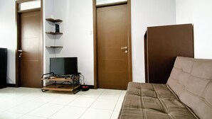A living room with a brown sofa, a TV on a stand, and two doors. - Homey and Cozy Living 2BR Lagoon Bekasi Town Square Apartment (Bekasi)