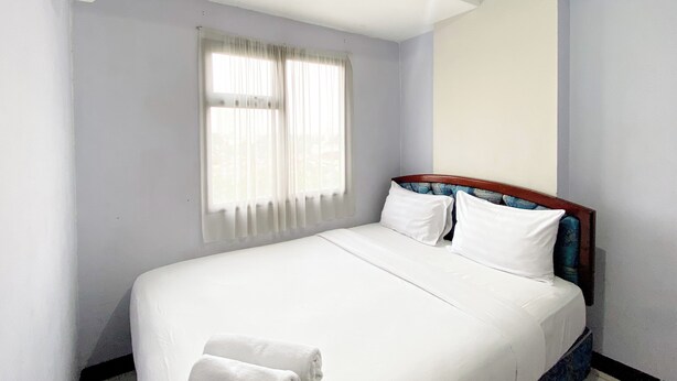A hotel room with a single bed, a window with sheer curtains, and a ceiling-mounted air conditioner. - Homey and Cozy Living 2BR Lagoon Bekasi Town Square Apartment (Bekasi)