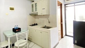 A compact kitchen with white cabinets, a gas stove, a sink, and a small table with chairs. - Homey and Cozy Living 2BR Lagoon Bekasi Town Square Apartment (Bekasi)