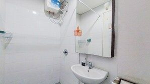 Un baño con lavamanos blanco, un espejo, un secador de manos y una pequeña estantería con artículos de aseo.