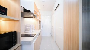 A modern kitchen with white cabinetry, a black microwave, and a stainless steel range hood. - Cozy Studio Connected To Mall At The Vertu Apartment (Surabaya)