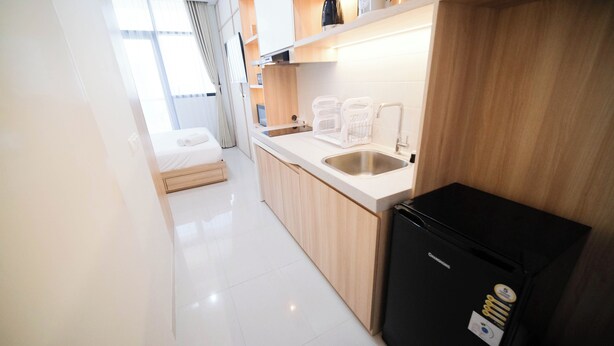 A compact kitchen with a sink, a black refrigerator, and a bed in the background. - Cozy Studio Connected To Mall At The Vertu Apartment (Surabaya)