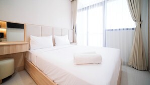 A hotel room with a large bed, a bedside table, a mirror, and a window with curtains. - Cozy Studio Connected To Mall At The Vertu Apartment (Surabaya)
