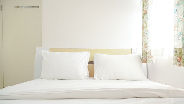 A neatly made bed with white linens and a wooden headboard.
