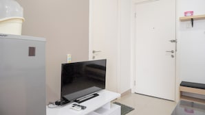 A room with a white door, a white cabinet, a flat-screen TV, and a small shelf with a pink box.
