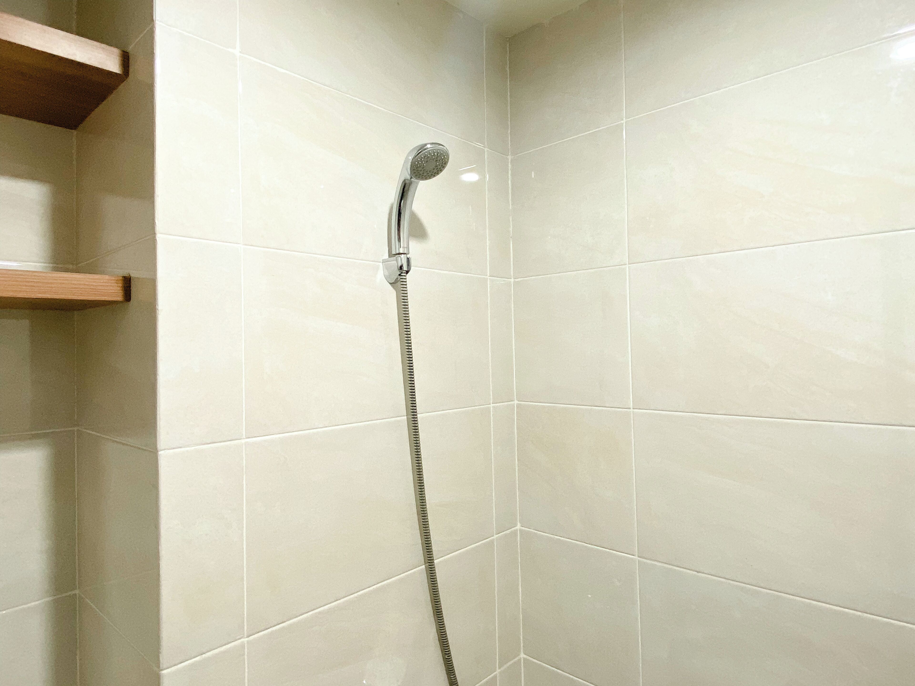 A shower with a handheld showerhead and a flexible hose, tiled walls, and a wooden shelf.