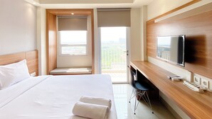Een hotelkamer met een groot bed, een bureau met een televisie, en een balkon met uitzicht op de stad.