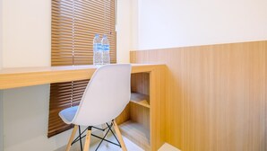 Een werkplek met een houten bureau, een witte stoel en een raam met zonwering.