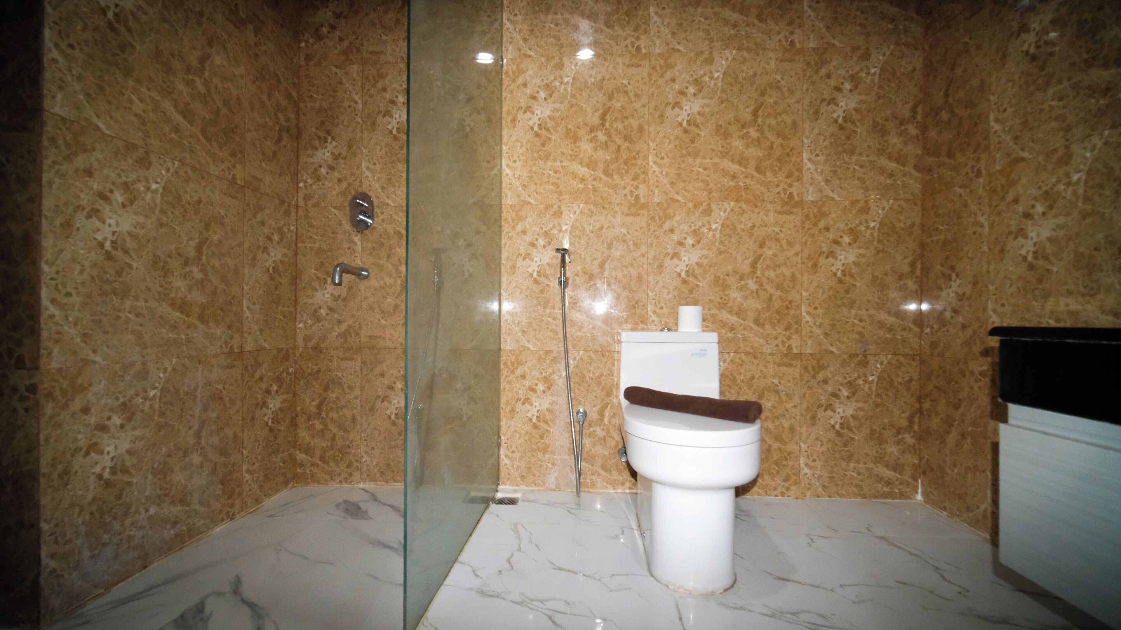 A bathroom with a glass shower enclosure, a toilet, and marble flooring.
