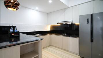A modern kitchen with a black countertop, stainless steel appliances, and a geometric pendant light.
