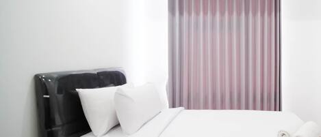 Una habitación de hotel con una cama, almohadas, un cabecero negro y un ventanal con cortinas.