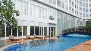 A modern hotel with a swimming pool, lounge chairs, and a stone bridge. - Exclusive And Spacey 3Br At Grand Sungkono Lagoon Apartment (Surabaya)