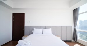 A hotel room with a bed, a door, a nightstand, and a window with curtains.