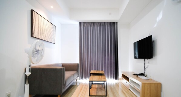 A modern living room with a sofa, a small wooden table, a TV, and a wall-mounted fan.