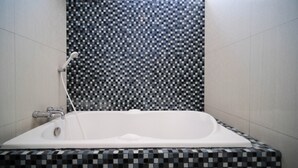 Ein modernes Badezimmer mit Wandgestaltung aus Schachbrettmuster-Mosaik, einer weißen Badewanne und einer sichtbaren Duschbrause.