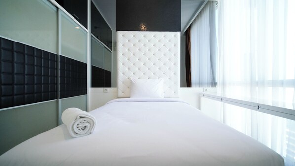 A modern hotel room with a large bed, a tufted headboard, a mirror, and a view of the city through large windows.