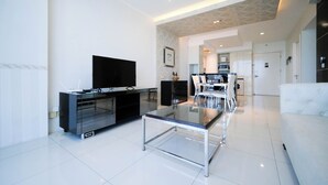 Ein modernes Wohnzimmer mit Flachbildfernseher, einem Glastisch und einer Essecke mit Stühlen und Tisch.