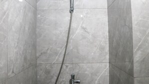 A shower with a handheld showerhead and a flexible hose, set in a room with large, glossy marble tiles. - Simply Look And Comfy Studio Sayana Bekasi Apartment (Tarumajaya)