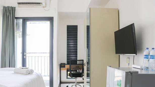 A hotel room with a bed, a desk, a chair, a television, and a refrigerator. - Simply Look And Comfy Studio Sayana Bekasi Apartment (Tarumajaya)
