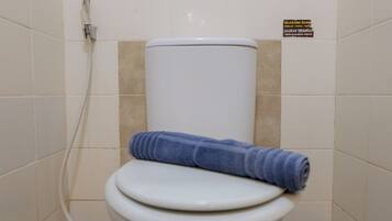 Des toilettes avec une serviette bleue posée sur le siège, un tuyau d’eau et un panneau sur le mur.