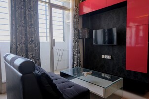 Un salon moderne avec une table basse en verre, un canapé noir et un mur d’accent rouge.