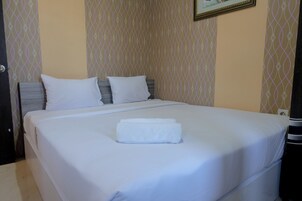 Una cama bien hecha con sábanas y almohadas blancas, una toalla doblada sobre la cama, y un papel tapiz estampado en las paredes.