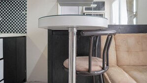A modern bar stool with a glass top and metal legs, positioned in a room with a beige sofa and a checkered wall pattern. - Cozy Stay 1Br At Green Pramuka City Apartment (Jakarta)
