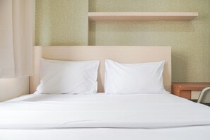A neatly made bed with white linens and two pillows, a wooden headboard, and a small bedside table with a lamp.