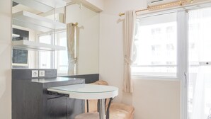 A modern bathroom with a glass sink, a beige cushioned bench, a large mirror, and a sliding glass door to the outside. - Cozy Stay 1Br At Green Pramuka City Apartment (Jakarta)