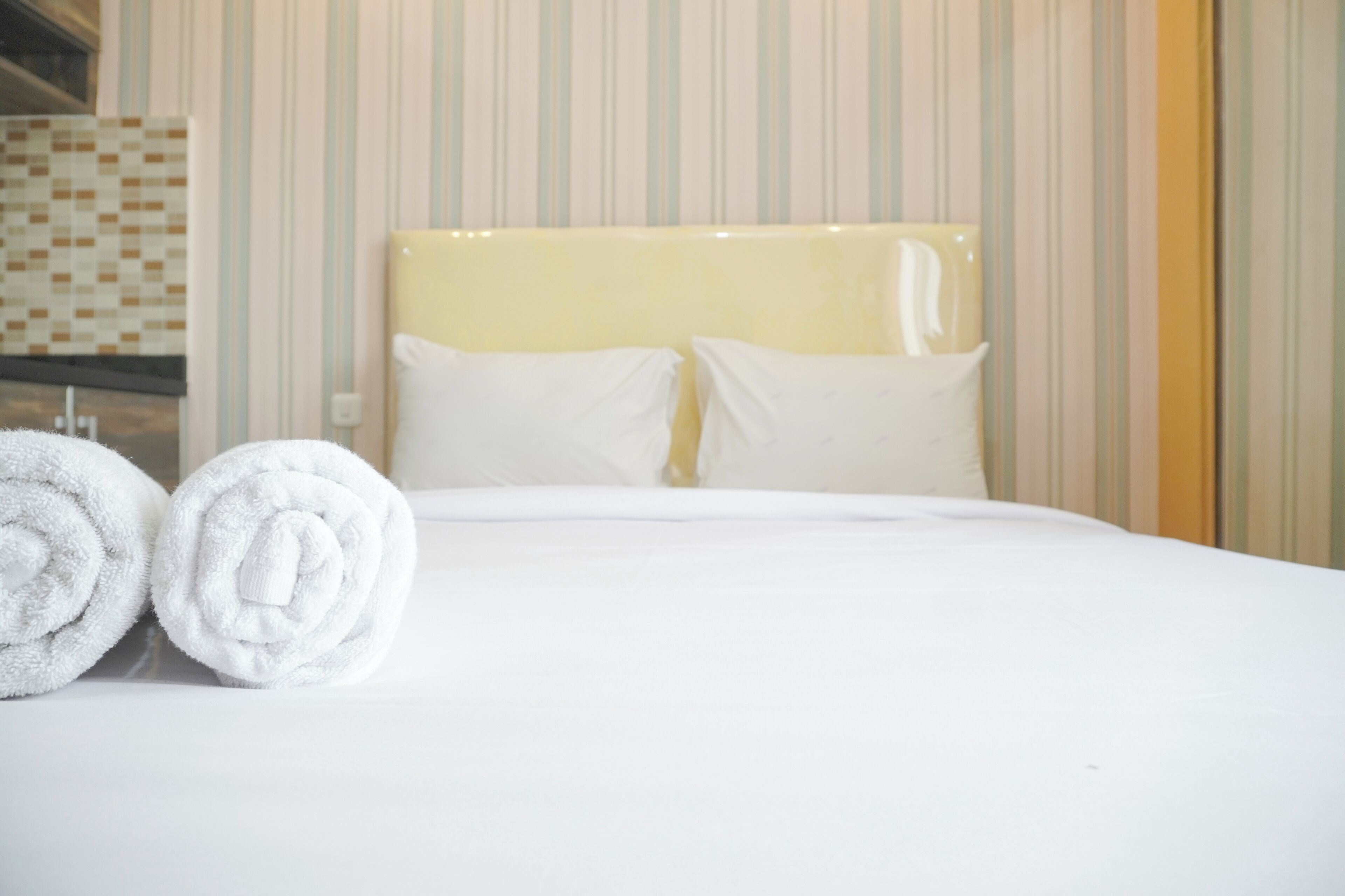 Een opgemaakt bed met witte lakens en twee opgerolde handdoeken.