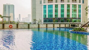 Une piscine équipée d’une bouée de sauvetage, entourée d’un petit muret et de plantes. Au fond, on aperçoit des bâtiments modernes dotés de grandes fenêtres.