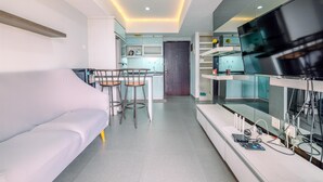 Un salon moderne comprenant un canapé, un coin repas avec des tabourets, un espace cuisine et un téléviseur fixé au mur.