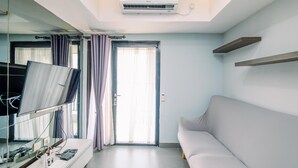 Un salon moderne doté d’un téléviseur à écran plat, d’un canapé, d’un climatiseur fixé au plafond et d’une grande fenêtre avec des rideaux.