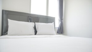 A neatly made bed with white linens and pillows, a grey headboard, and a window with curtains. - Nice And Tidy 2Br At Bassura City Apartment Near Mall (Jakarta)