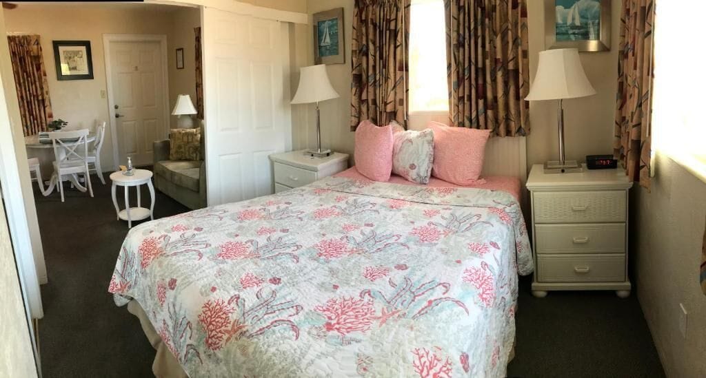 A bedroom with a bed, two bedside tables, a nightstand, a chair, and a desk.