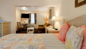 A hotel room with a bed, a desk, a chair, a television, and a lamp.